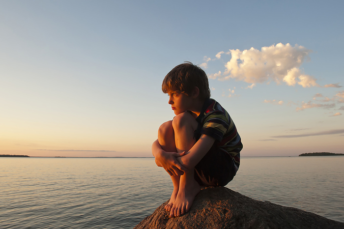 Young boy looking out over a lake at dusk, Leech Lake near Walker, Minnesota, USA; Walker, Minnesota, United States of America, by Joel Sartore Photography / Design Pics