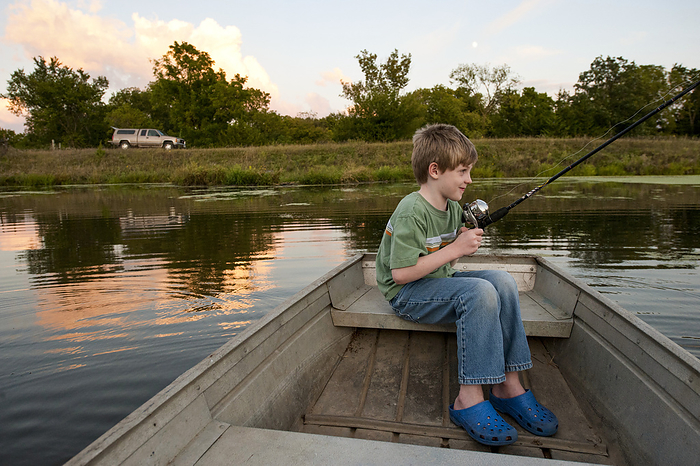 Young boy anticipates catching a fish in a pond from a boat at dusk; Ceresco, Nebraska, United States of America, by Joel Sartore Photography / Design Pics