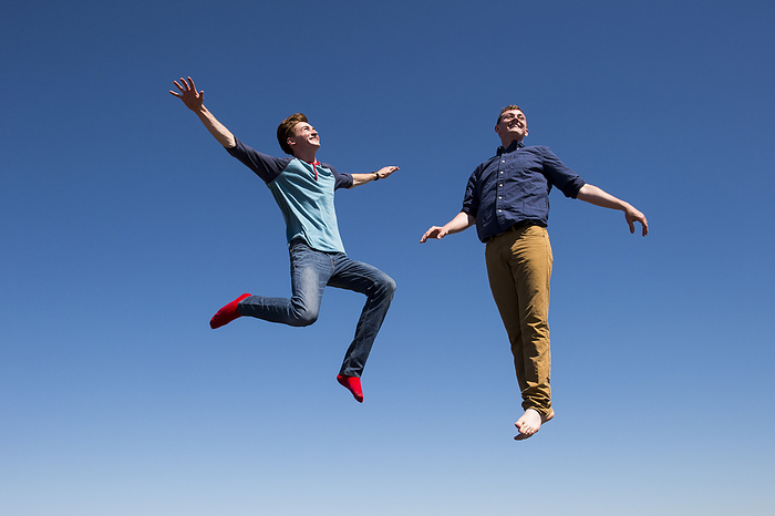 Two young men in mid-air against a blue sky as they jump on a trampoline; Bennet, Nebraska, United States of America, by Joel Sartore Photography / Design Pics