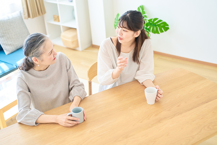 A senior woman and a young Japanese woman talking amicably in their room (People)
