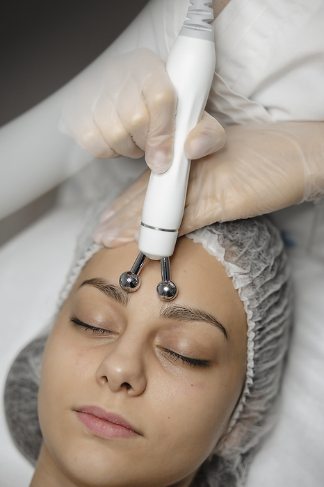 Hands of dermatologist massaging with equipment on woman's forehead