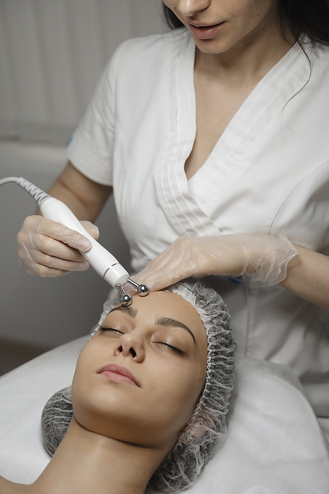 Young dermatologist massaging with equipment on woman's forehead