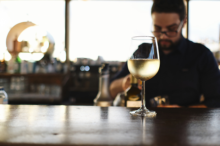 Glass of white wine on table with bartender in background
