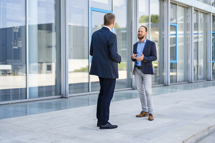 Two businessmen standing in front of office building talking