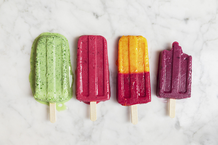 Homemade berry fruit popsicles flat laid against marble background