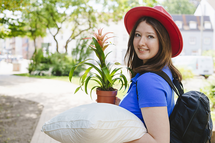 Smiling teenage girl carrying potted plant and pillow
