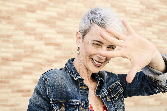 Smiling woman showing stop gesture in front of wall