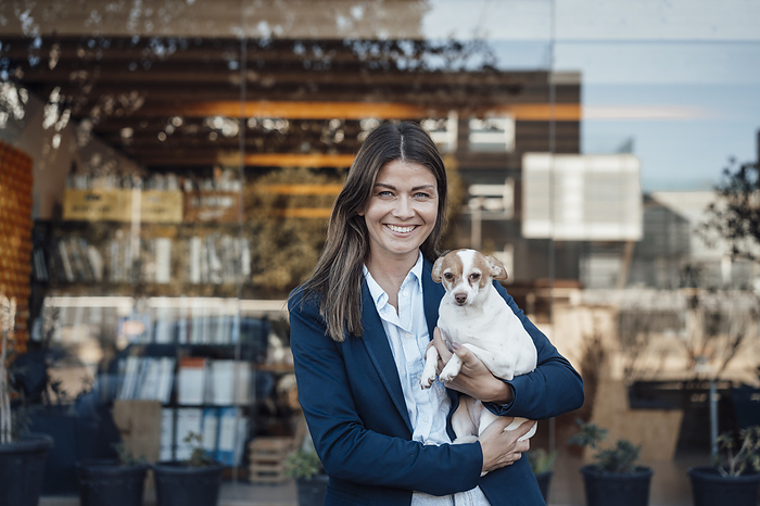 Happy businesswoman holding dog in front of glass