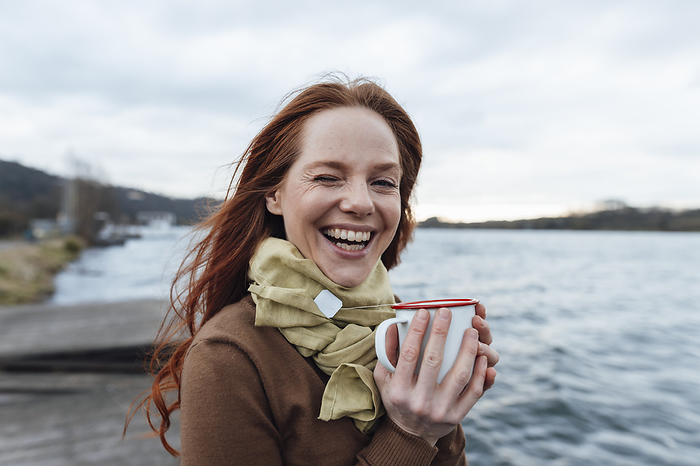 Happy woman with tea cup by lake