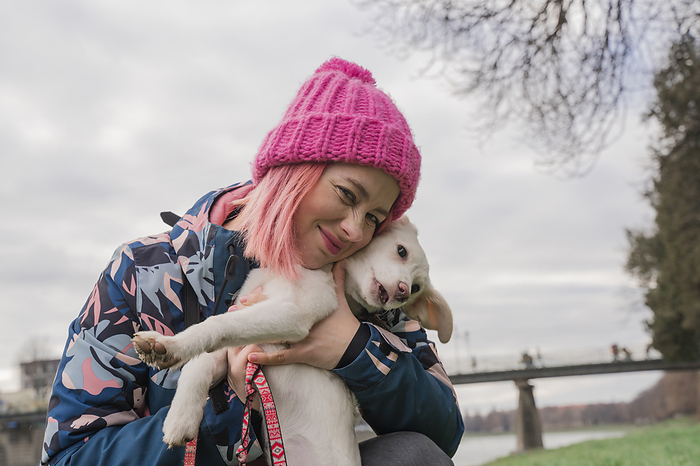 Happy woman wearing knit hat hugging dog in garden