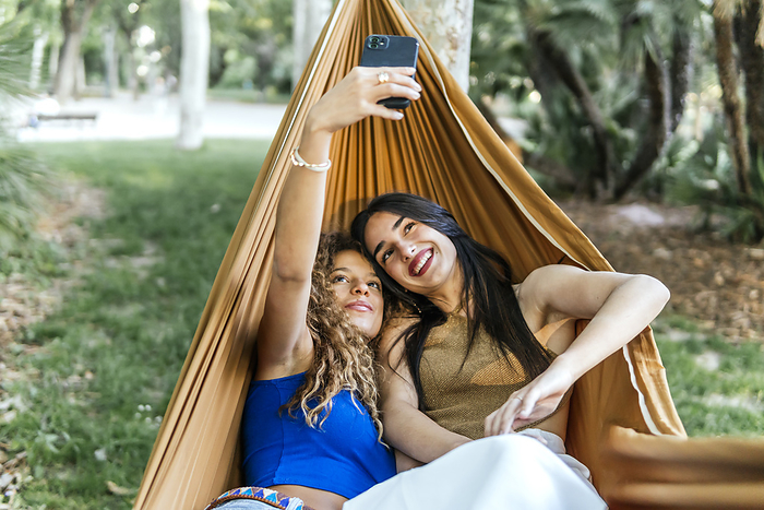 Lesbian couple taking selfie on smart phone in hammock