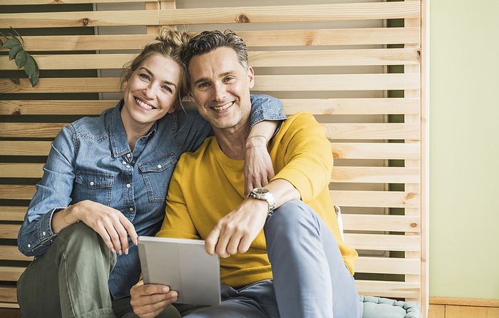 Portrait of couple sitting together in front of wooden bed frame leaning on wall