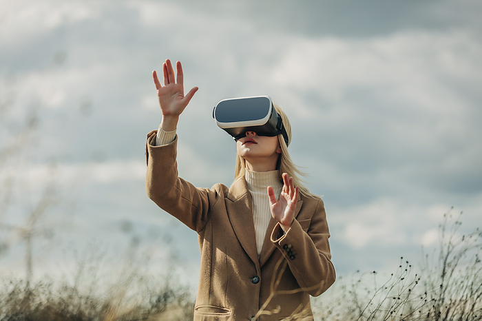 Woman gesturing with virtual reality simulators under cloudy sky
