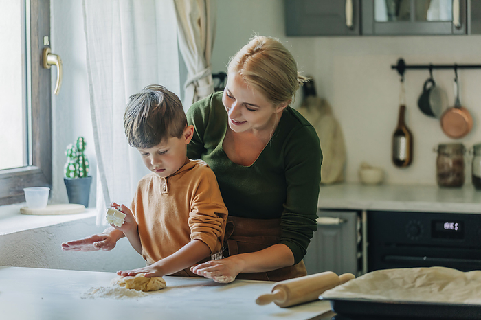 Mother and son kneading dough in kitchen at home