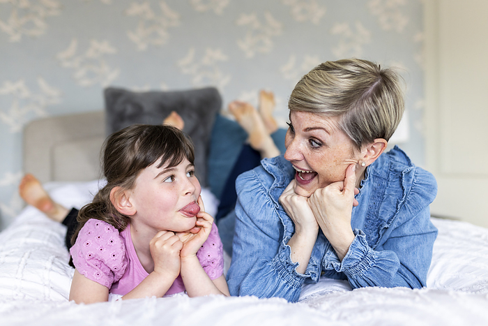 Cheerful mother and daughter making facial expression lying on bed