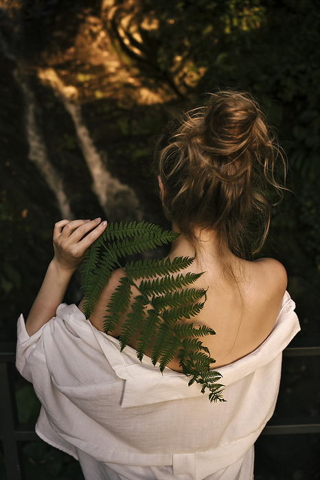 Young woman holding fern leaf on shoulder at sunset