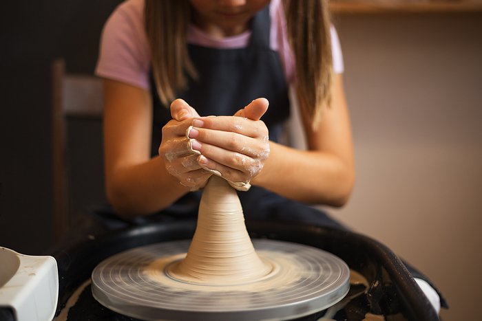 A girl working with clay on a Potter's wheel close up. Tradition, by Cavan Images / Galina Oleksenko