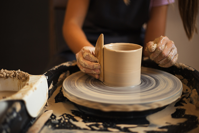 Close up of teenage girl's hands molds clay pot spinning on pott, by Cavan Images / Galina Oleksenko