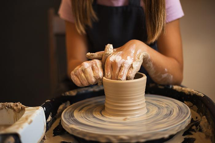 Close up of teenage girl's hands modeling pottery on a potter wh, by Cavan Images / Galina Oleksenko
