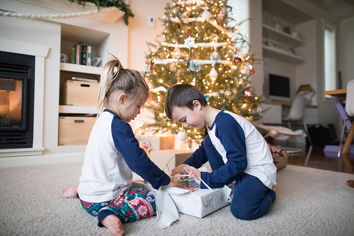 brother and sister work together to unwrap christmas gifts, by Cavan Images / Christopher Kimmel / Alpine Edge Photography
