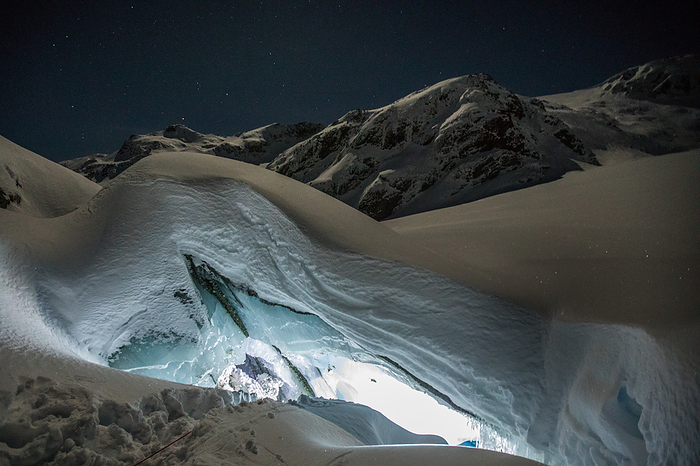Illuminated cave entrance in mountains, winter season, by Cavan Images / Christopher Kimmel / Alpine Edge Photography