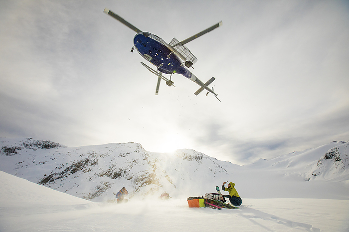 Helicopter flying in mid-air above two passengers ready for pick up, by Cavan Images / Christopher Kimmel / Alpine Edge Photography