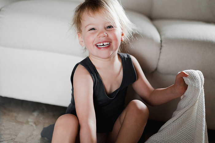 Playful shaggy baby girl laughs merrily while sitting on the floor, by Cavan Images / Liza Zavialova