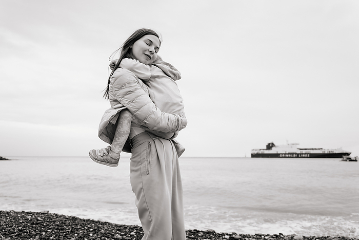 Woman hugging her child tightly on a pebble beach, BW, by Cavan Images / Liza Zavialova