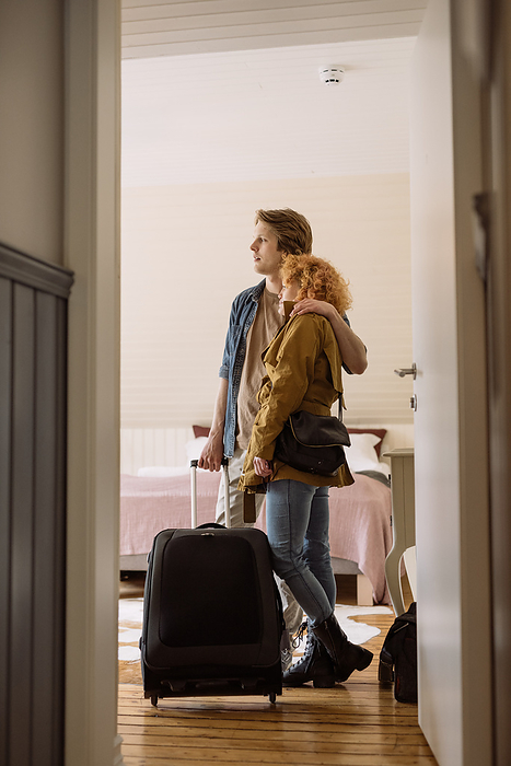 Happy couple with suitcase standing in hotel room, by Cavan Images / Oscar Bjarnason