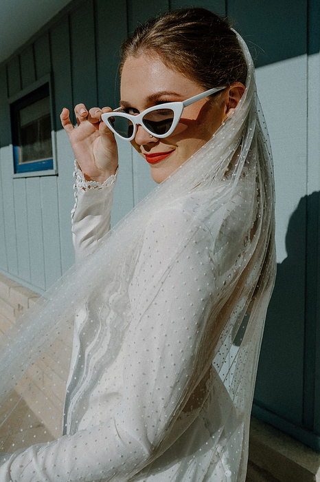 Retro bride tips sunglasses, in vintage gown and red lipstick., by Cavan Images / Ashlyn Peters