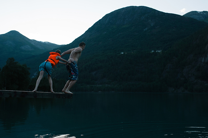 son pushing his father off a diving board into a Norwegian Fjord, by Cavan Images / Rachel Bell