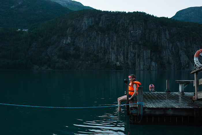 girl sat on a dock waiting to swim in a Norwegian Fjord, by Cavan Images / Rachel Bell
