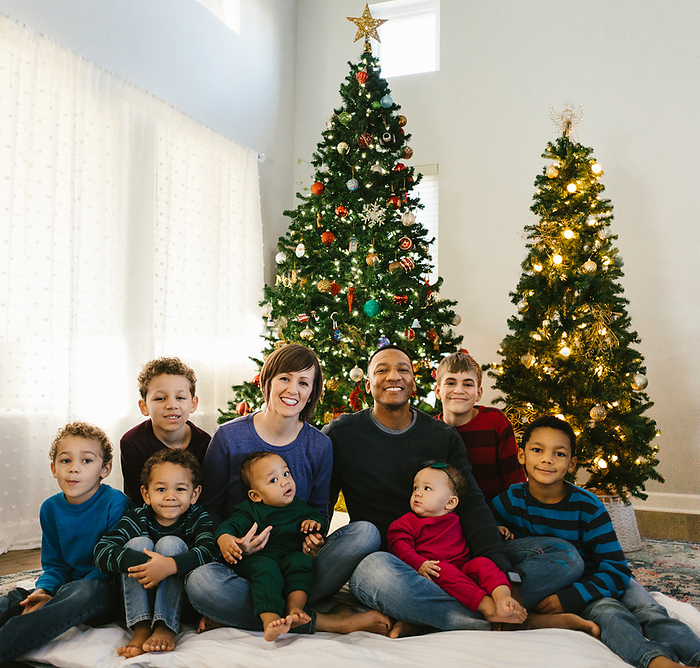 Diverse family together under Christmas trees in their home, by Cavan Images / Anna Rasmussen Photographs