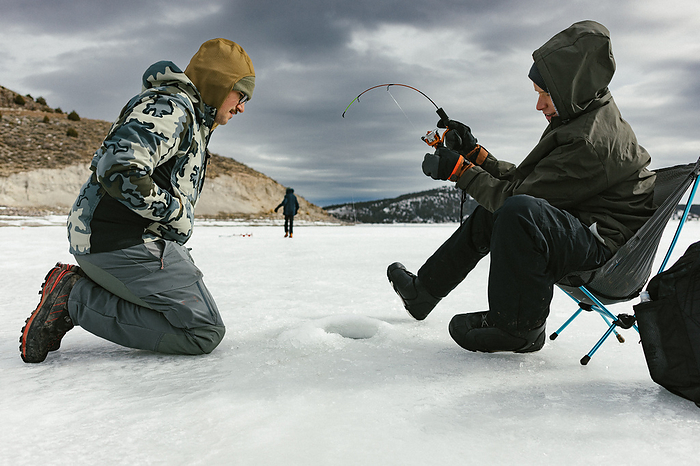 Family ice fishes in winter outdoor adventure on frozen lake, by Cavan Images / Anna Rasmussen Photographs