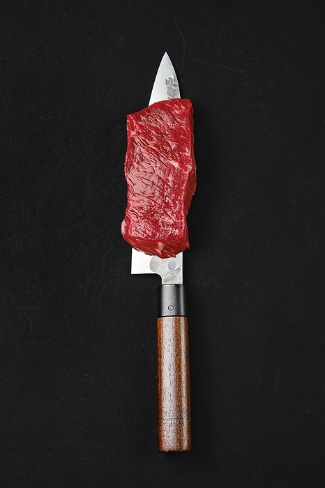 Piece of raw strip steak on the blade of knife, by Aleksei Isachenko