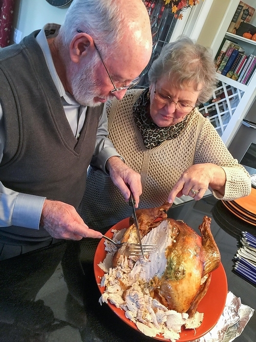 Senior adult couple cutting the holiday Turkey together in the kitchen, by Andy Dean