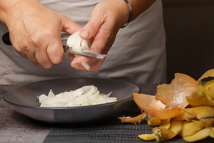 Close-up of a woman's hands in a white apron peeling onion with a knife, by jose hernandez antona