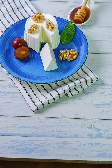 Fresh cheese with walnuts on a blue plate on a wooden table and copy space, by jose hernandez antona