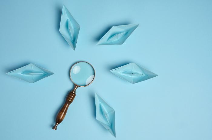 Blue paper boats and a magnifying glass, viewed from above Blue paper boats and a magnifying glass, viewed from above