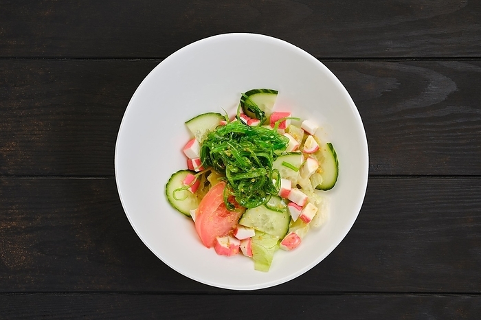 Salad with crab meat, seaweed, tomato, cucumber and sesame on dark wooden table