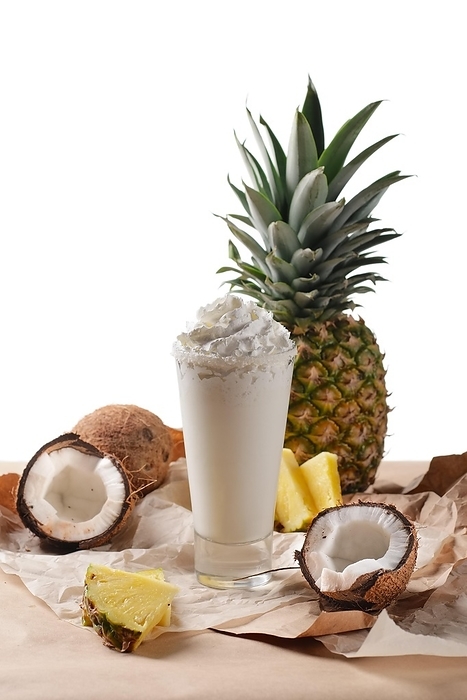 Selective focus composition with coconut cocktail served with pineapple and coconuts on rough paper over the wooden table