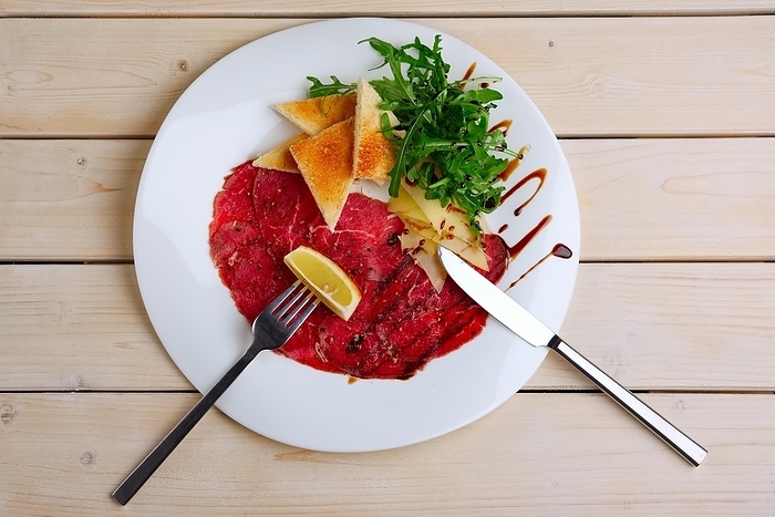 Top view of plate with beef carpaccio with cheese, white bread toasts and lemon on fork