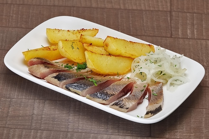 Plate with pickled herring and onion with potato wedges on wooden table