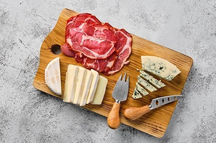 Top view of wooden cutting board with smoked bacon, brie cheese and gorgonzola