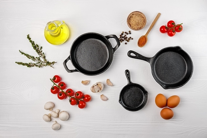 Cast iron skillets and spices on white wooden culinary background, view from above