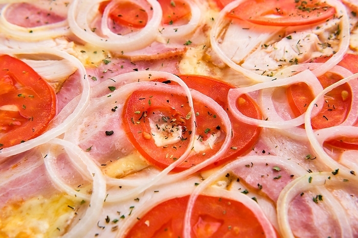 Macro photo of tomato, ham, bacon, onion and cheese on pizza (photo with shallow depth of field)