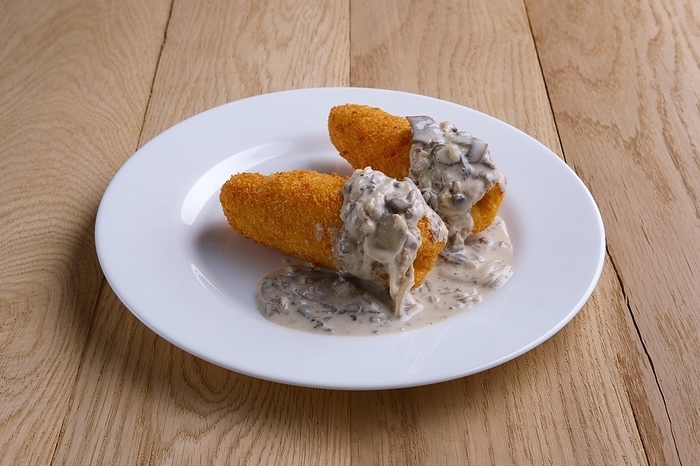 Potato cutlet in breading stuffed with ham served with mushroom sauce on wooden table