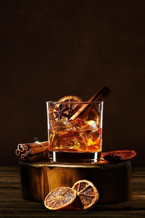 Cold cocktail with bourbon and orange liquor, cinnamon and star anise on wooden log