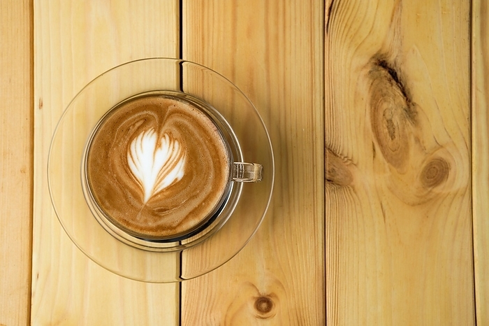 Overhead view of cappuccino in transparent glass cup on wooden table