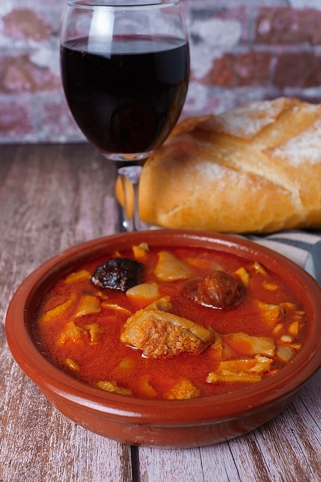 Clay casserole with Madrid-style stewed tripe, typical spanish food on a wooden table with a brick wall in the background